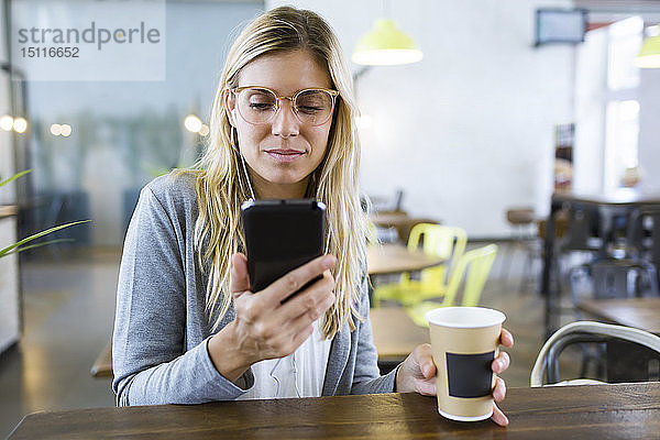 Junge Frau schreibt mit ihrem Handy SMS  während sie im Café Kaffee trinkt
