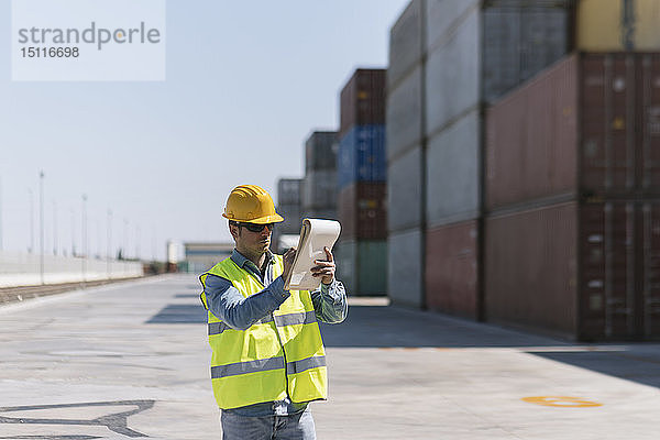 Arbeiter mit einem Notizblock in der Nähe von Frachtcontainern auf einem Industriegelände