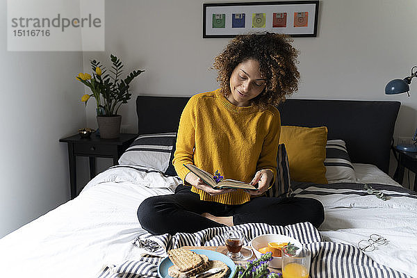 Frau sitzt im Bett  frühstückt gesund  liest Buch