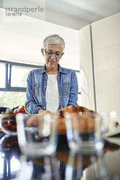 Ältere Frau steht in der Küche und schneidet Erdbeeren