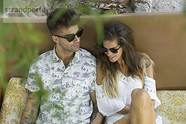 Entspanntes junges Paar mit Sonnenbrille sitzt im Freien