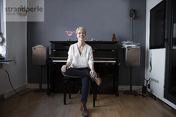 Porträt einer entspannten Frau  die in ihrem Musikzimmer vor dem Klavier sitzt