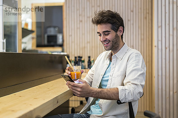 Mann mit Handy am Tresen einer Bar bei einem Drink