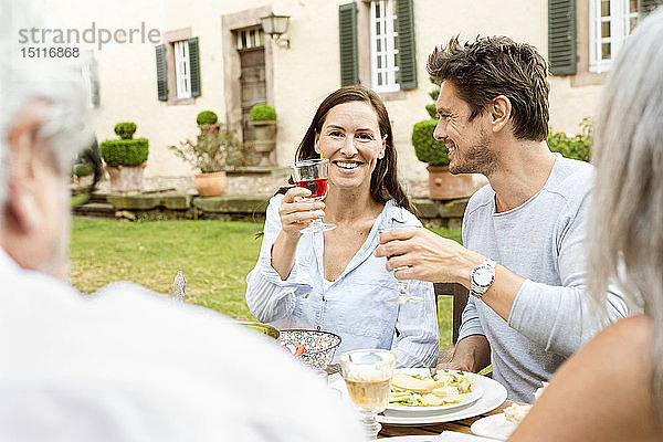 Fröhliche Familie beim gemeinsamen Essen im Garten  anstoßend