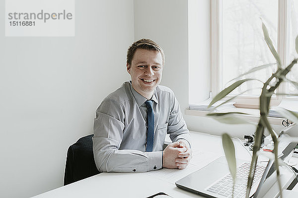 Porträt eines lächelnden jungen Geschäftsmannes  der im Büro am Schreibtisch sitzt