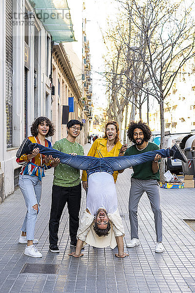 Freunde halten Mann beim Handstand auf Bürgersteig in der Stadt