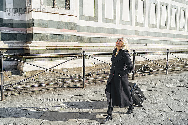 Italien  Florenz  reife Geschäftsfrau in schwarzem Mantel  die mit einem Rollkoffer durch die Stadt läuft