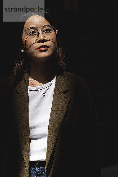 Porträt einer jungen Frau mit Brille  die sich im Sonnenlicht umsieht