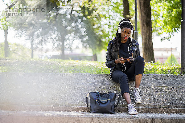 Frau ruht sich im Stadtpark mit Handy und Kopfhörern aus