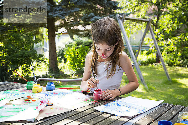 Kleines Mädchen malt bei Tisch im Garten