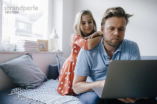 Mädchen beobachtet Vater am Laptop zu Hause