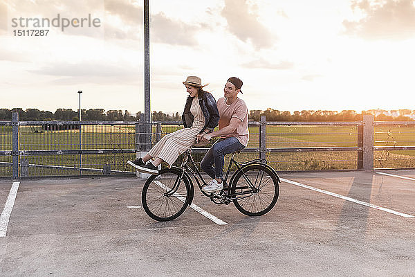 Glückliches junges Paar zusammen auf einem Fahrrad bei Sonnenuntergang auf dem Parkdeck
