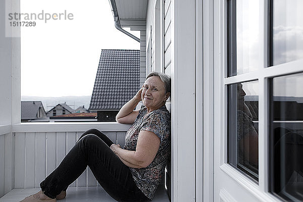 Porträt einer lächelnden  entspannten älteren Frau  die auf der Veranda sitzt