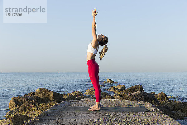 Junge Frau  die am Strand Yoga praktiziert und Sonnengrüße ausspricht