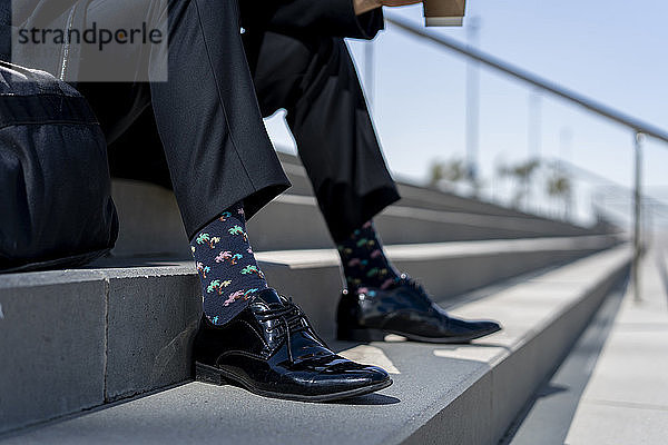 Nahaufnahme eines Geschäftsmannes  der auf einer Treppe sitzt und gemusterte Socken trägt