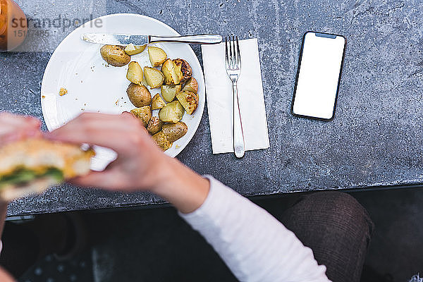 Nahaufnahme eines Mannes  der einen Veganer-Burger mit Kartoffeln zum Mittagessen isst