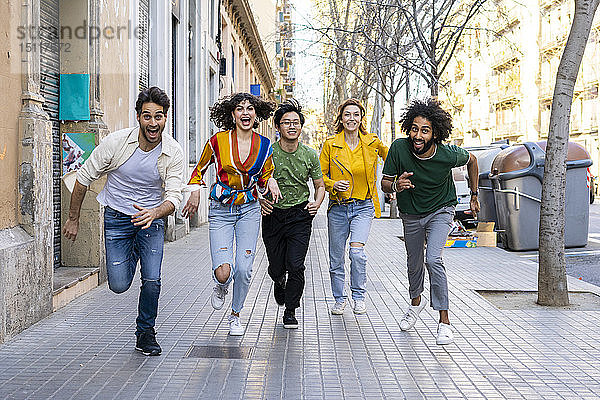 Glückliche Gruppe von Freunden amüsiert sich in der Stadt beim Laufen auf dem Bürgersteig