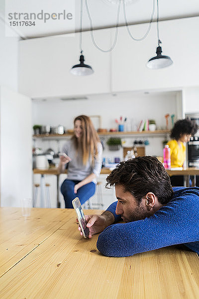 Mann benutzt Handy am Esstisch zu Hause mit Freunden im Hintergrund