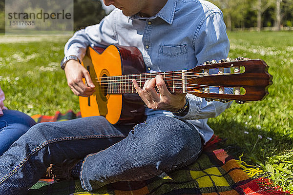 Junger Mann spielt Gitarre in einem Park