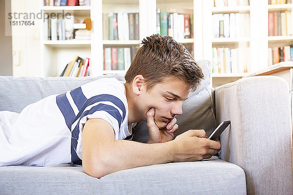 Teenager  der zu Hause auf der Couch liegt und sein Handy benutzt