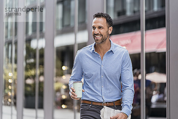 Geschäftsmann mit Kaffee und Zeitung zum Mitnehmen in der Stadt unterwegs