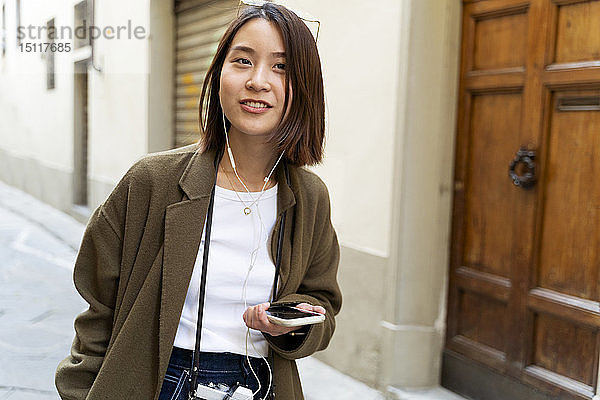 Italien  Florenz  junge Frau mit Kopfhörern und Handy in einer Gasse