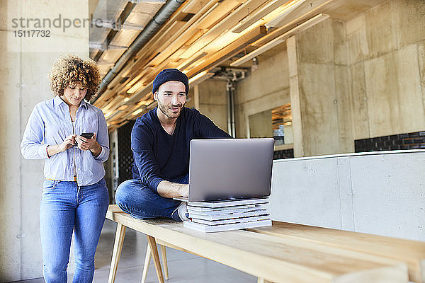 Frau mit Handy und Mann mit Laptop im modernen Büro