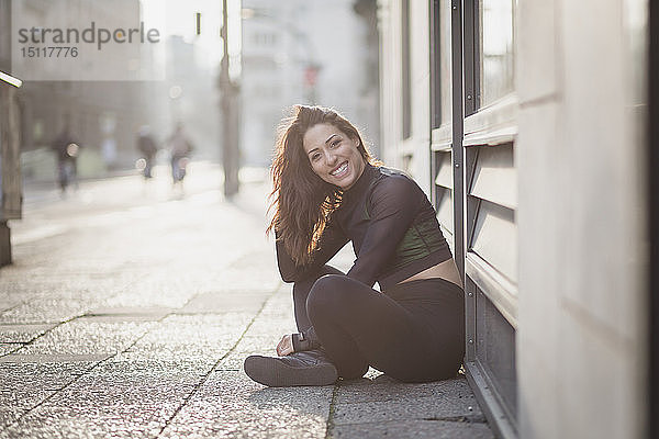 Porträt einer glücklichen  sportlichen jungen Frau  die in der Stadt auf dem Boden sitzt