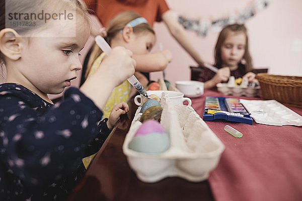 Mädchen malen zu Hause Ostereier auf den Tisch