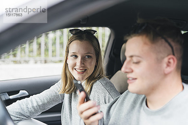 Porträt einer jungen Frau in einem Auto  die ihren Freund auf dem Fahrersitz mit einem Smartphone beobachtet
