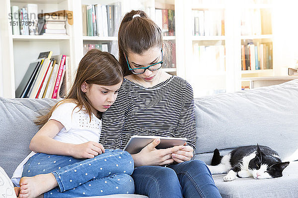 Zwei Schwestern sitzen zu Hause auf der Couch und schauen mit einem digitalen Tablet einen Film an