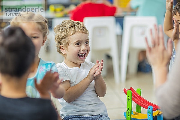 Glückliche Kinder und Vorschullehrerin klatschen im Kindergarten in die Hände