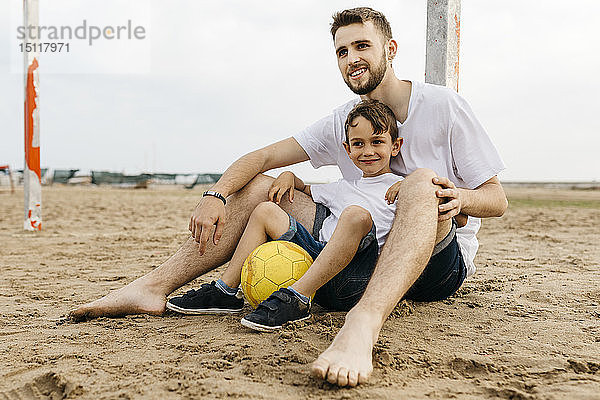 Mann und Junge ruhen sich nach Fußballspiel am Strand aus