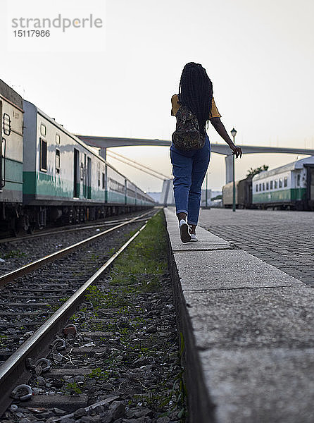 Rückansicht einer jungen Frau  die am Rande des Bahngleises am Bahnhof geht