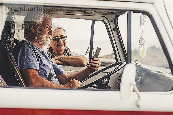 Älteres Ehepaar reist in einem Oldtimer-Van und benutzt ein Smartphone