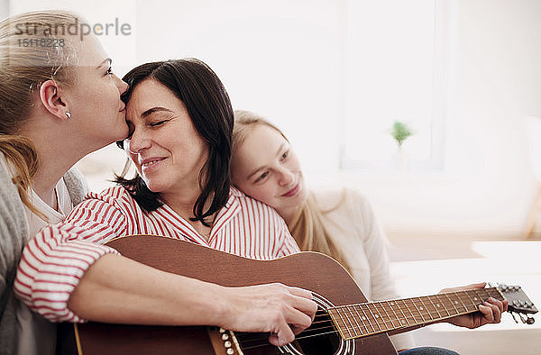 Reife Frau mit zwei liebevollen Töchtern  die zu Hause Gitarre spielen
