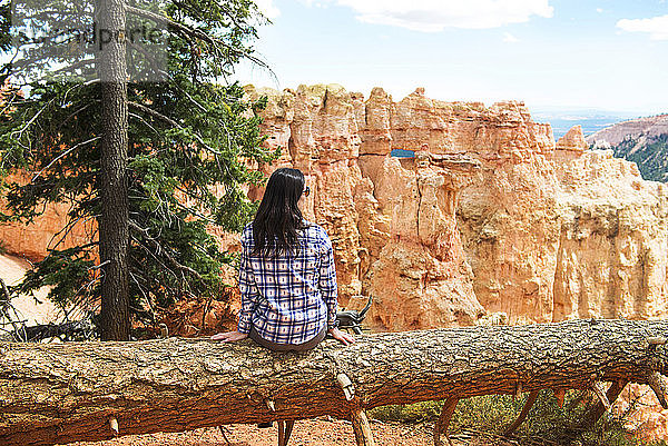 Reisende Frau sitzt auf dem Stamm eines umgefallenen Baumes und genießt die Aussicht im Bryce Canyon  Utah  USA