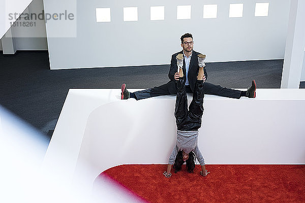 Amtierender Geschäftsmann hält Frauenbeine beim Handstand