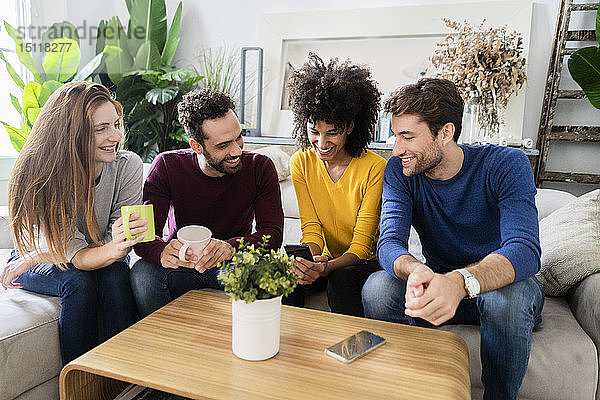 Vier glückliche Freunde sitzen auf der Couch und telefonieren