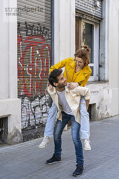 Mann nimmt seine Freundin huckepack auf dem Bürgersteig in der Stadt