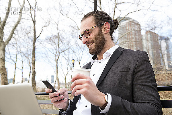 Lächelnder junger Geschäftsmann mit Kaffee zum Handybesuch  New York City  USA