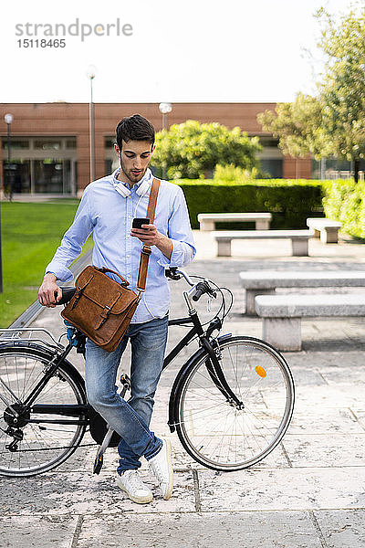 Junger Mann mit Fahrrad und Smartphone  Kopfhörer um den Hals in der Stadt