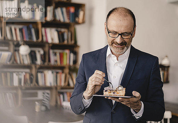 Ein reifer Geschäftsmann mit einem Stück Kuchen auf einem digitalen Tablet in einem Cafe