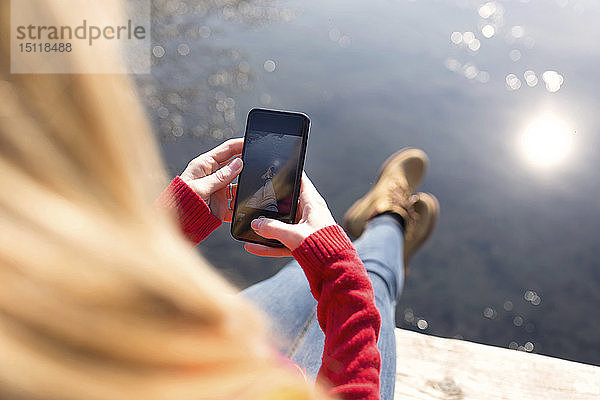 Junge blonde Frau benutzt im Winter ein Smartphone an einem See