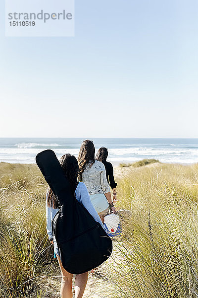 Rückansicht von Frauen mit Gitarrentasche  die in den Dünen Richtung Strand laufen