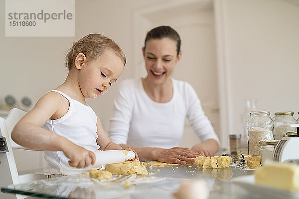 Mutter und kleine Tochter mit Teigrolle  die zu Hause in der Küche gemeinsam einen Kuchen backen
