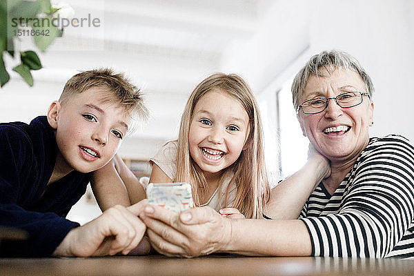 Porträt der glücklichen Grossmutter und Enkelkinder mit Handy zu Hause