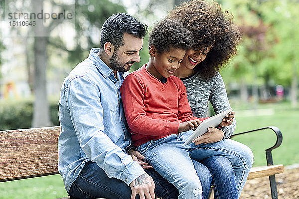 Familie sitzt auf einer Parkbank und verwendet ein digitales Tablett