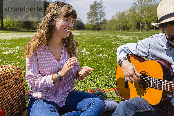 Junger Mann spielt Gitarre für seine Freundin in einem Park