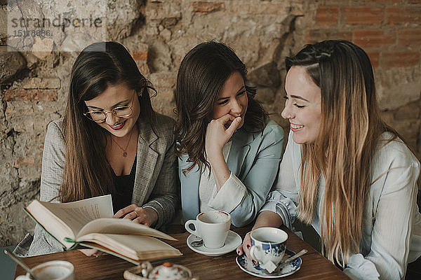 Drei glückliche junge Frauen lesen ein Buch in einem Café